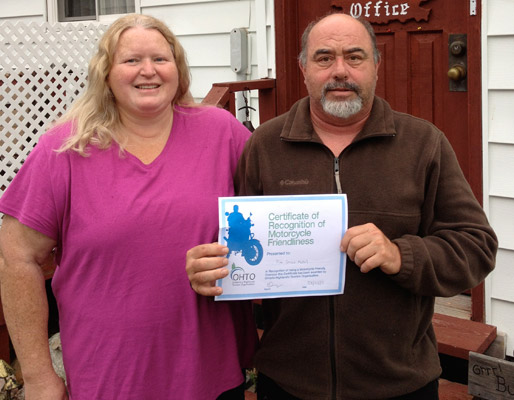 a couple standing in front of a red door holding a motorcycle friendliness certificate