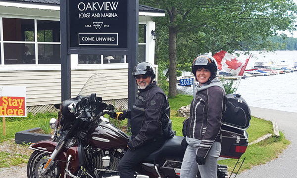  Two people with motorcycle in front of the Oakview Lodge and Marina sign and lake