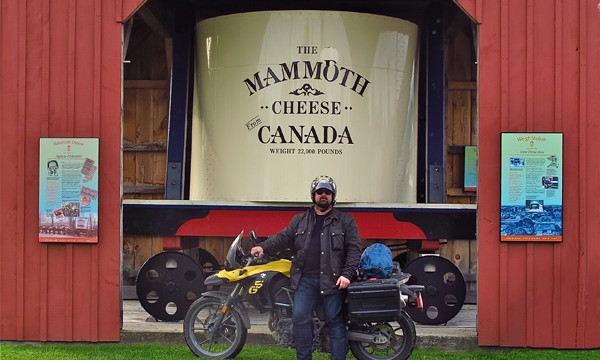 Man with motorcycle standing in front of mammoth cheese monument