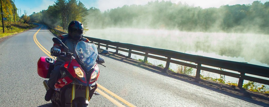 Motorcycle riding past a misty lake.
