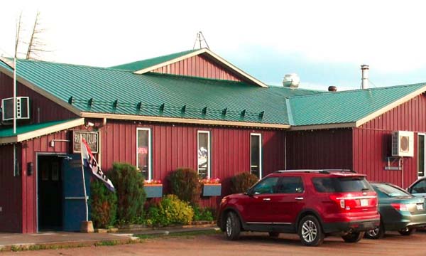 Restaurant with red siding and a green roof. Red, green and silver cars parked in front of restaurant.